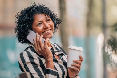 Sokakta oturan bir kadın cep telefonuyla konuşuyor.