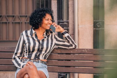 Sokakta oturan mutlu kadın cep telefonuyla konuşuyor.