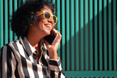 Sokakta gülümseyen, güneş gözlüklü bir kadın cep telefonuyla konuşuyor.