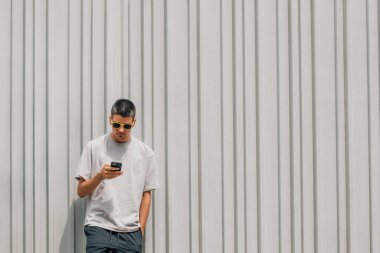 Yazın sokakta duvarda cep telefonu ve güneş gözlüğü olan bir çocuk.