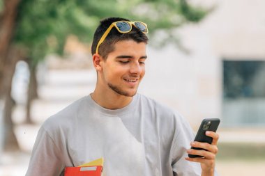 Kampüste ya da açık havada kitapları ve cep telefonu olan bir öğrenci.