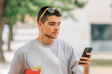 Kampüste ya da açık havada kitapları ve cep telefonu olan bir öğrenci.
