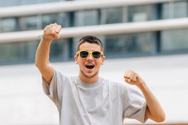 Dışarıda güneş gözlüklü genç adam sevinçle kutluyor.