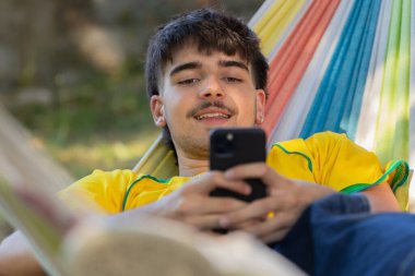 Hamaktaki cep telefonlu genç erkek.