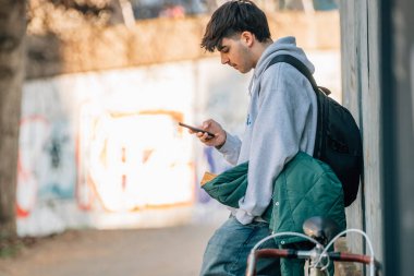 Duvarda cep telefonu olan genç bir adam ve kopyalama alanı olan klasik bir bisiklet.