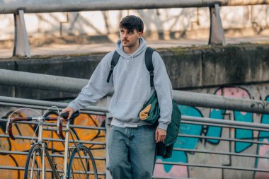 Bisiklet ve sırt çantasıyla yürüyen genç bir şehir kıyafeti.