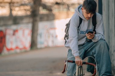 Genç şehir kıyafeti cep telefonuyla bisiklet sürüyor.