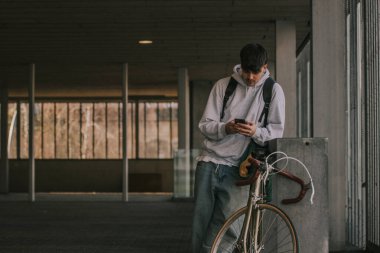 Cep telefonu ve klasik bisikleti olan genç yeraltı adamı, şehir manzarası