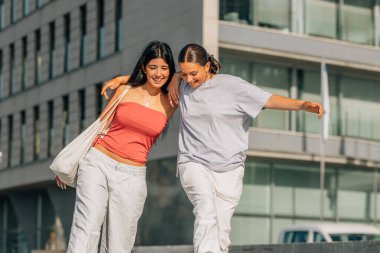 İki arkadaş sokakta kahkahalarla gülüyor.