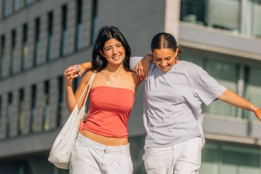 İki arkadaş sokakta kahkahalarla gülüyor.