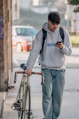 Sokakta cep telefonlu bir öğrenci klasik bir bisikletle yürüyor.