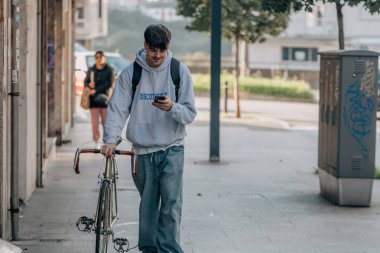 Sokakta cep telefonlu bir öğrenci klasik bir bisikletle yürüyor.