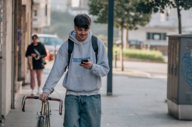 Sokakta cep telefonlu bir öğrenci klasik bir bisikletle yürüyor.