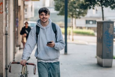 Sokakta cep telefonlu bir öğrenci klasik bir bisikletle yürüyor.