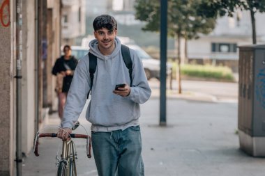 Sokakta cep telefonlu bir öğrenci klasik bir bisikletle yürüyor.