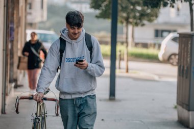 Sokakta cep telefonlu bir öğrenci klasik bir bisikletle yürüyor.