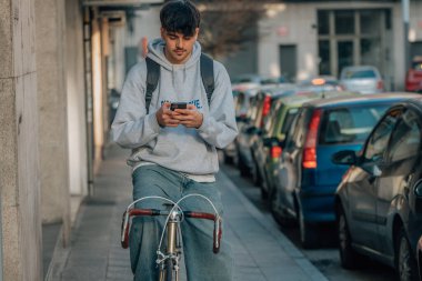 Sokakta cep telefonlu bir öğrenci klasik bir bisikletle yürüyor.