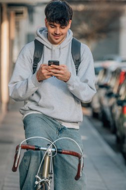 Sokakta cep telefonlu bir öğrenci klasik bir bisikletle yürüyor.