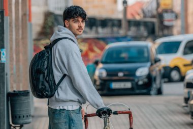 Sırt çantalı bisikletçi sokakta bisiklet taşıyor.