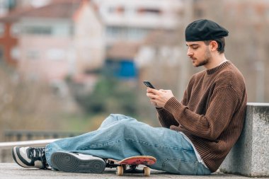 Sokaktaki genç adam cep telefonu ve kaykayıyla