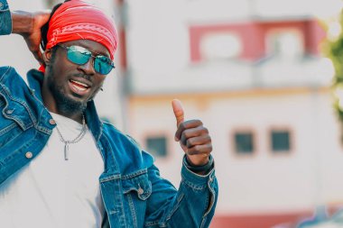 Genç Afrikalı adam güneş gözlüğü takıyor ve sokakta gündelik tarzda takılıyor.