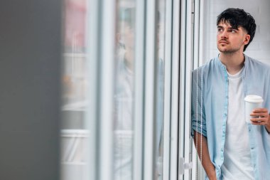 Evinin penceresinde fincanı olan genç adam