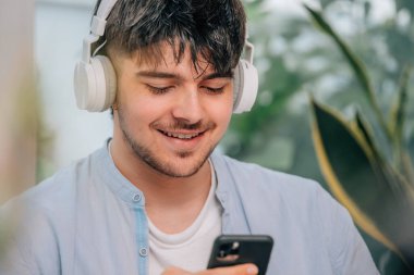Evde kulaklığı ve cep telefonu olan genç bir adam.