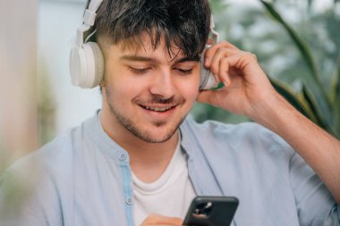 Evde kulaklığı ve cep telefonu olan genç bir adam.