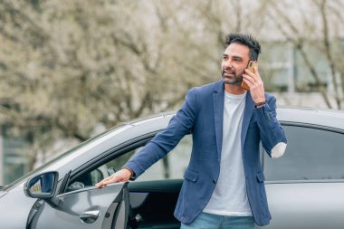 Genç bir adam ya da şoför arabadan çıkıp telefonuna ya da telefonuna bakıyor.