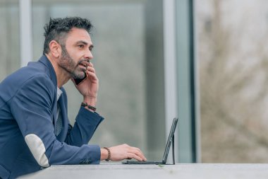Cep telefonu ve dizüstü bilgisayarı olan çekici bir iş adamı sokakta.