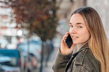 Sokaktaki sarışın kız cep telefonuyla konuşuyor.