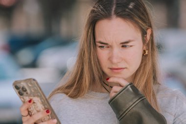 Caddedeki cep telefonuna düşünceli şüpheyle bakan bir kız.