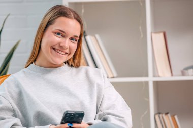 Evdeki kanepede oturan genç kadın cep telefonuyla.