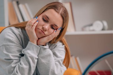 Genç bir kadın üzgün bir ifadeyle evdeki kanepede oturuyor.