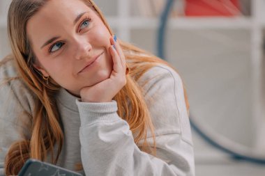 Evde cep telefonu olan sarışın bir kız ve şüpheli ve düşünceli bir yüz ifadesi var.