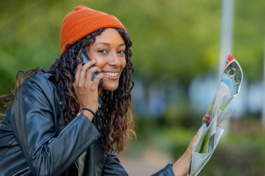 Sonbaharda harita ve cep telefonuyla seyahat eden genç bir kadın.