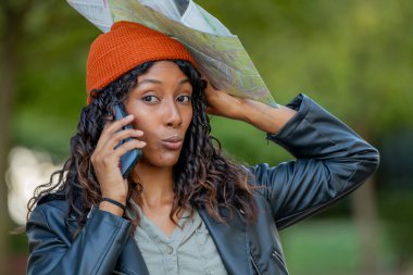 Sonbaharda harita ve cep telefonuyla seyahat eden genç bir kadın şaşırmış veya beklenmedik bir ifadeyle.