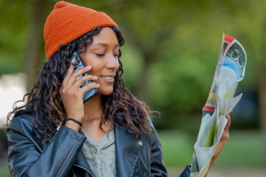 Sonbaharda harita ve cep telefonuyla seyahat eden genç bir kadın.