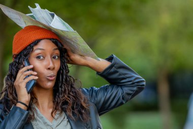 Sonbaharda harita ve cep telefonuyla seyahat eden genç bir kadın şaşırmış veya beklenmedik bir ifadeyle.