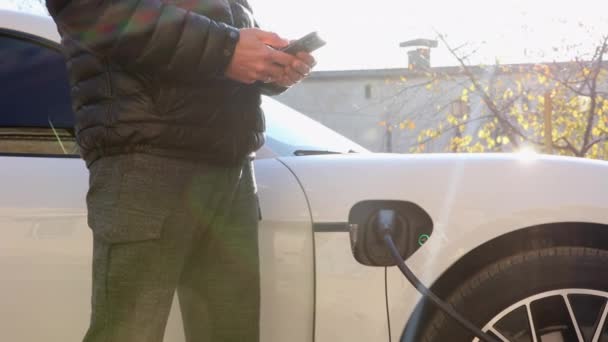 Facet Czarnej Kurtce Bierze Drogi Biały Elektryczny Samochód Ulicy Ładowania — Wideo stockowe