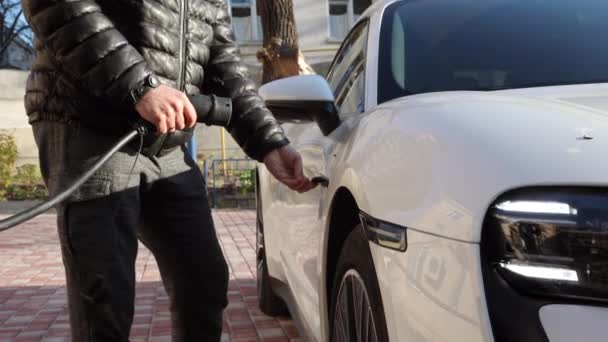 黒いジャケットの男が充電から路上で高価な白い電気自動車を充電します 高品質4K映像 — ストック動画