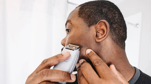 stock image African American man at home in bathroom cutting hair with clippers.