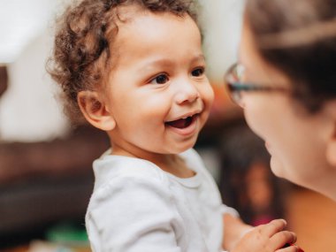 young millennial mother and diverse toddler boy with curly hair at home bonding together