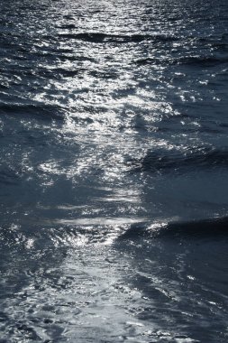 Ay ışığında denizde dalgalar var.