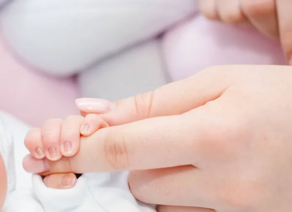 Newborn baby touching his mother hand. Mother uses her hand to hold her baby\'s tiny hand to make him feeling her love, warm and secure. Concept of child care, feeling safe, parent love.