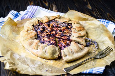 Siyah ahşap masanın üzerinde keten kumaş ve antika gümüş çatallı erikli meyveli turta crostata. Yemek fotoğrafçılığı