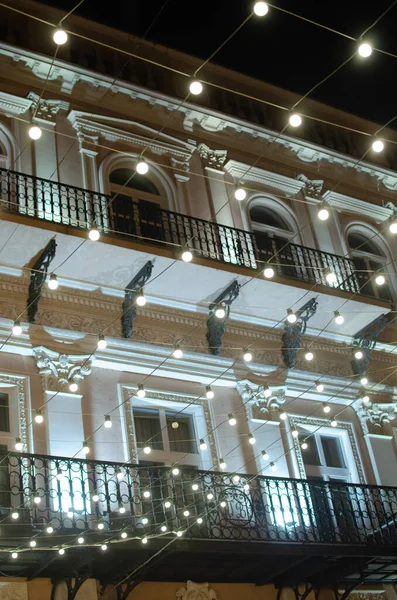 古典风格的历史建筑外观 白色和米黄色 高大的窗户 阳台与黑色金属栏杆 装饰灯泡 夜间城市摄影 — 图库照片