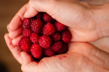 Bir avuç dolusu tatlı, olgun kırmızı ahududu yaz meyveleri kadın avuçlarında eller arka planda bulanık yemek fotoğraflarında.