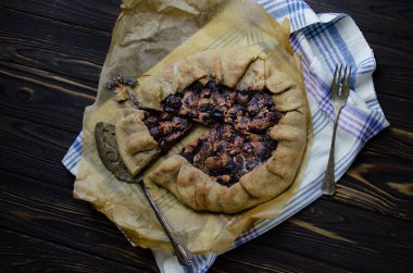 Siyah ahşap masanın üstünde erik meyveli turta crostata keten kumaş ve antika gümüş çatal bıçaklı pasta spatula yemek fotoğrafçılığı.