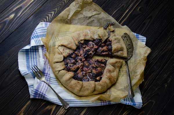 Siyah ahşap masanın üstünde erik meyveli turta crostata keten kumaş ve antika gümüş çatal bıçaklı pasta spatula yemek fotoğrafçılığı.